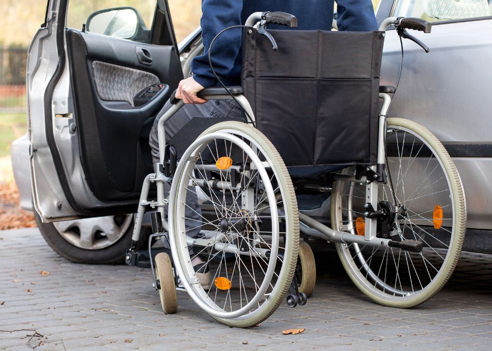 Displayed is a person in a wheelchair entering the driver's side of a car that's modified for people with paraplegia.