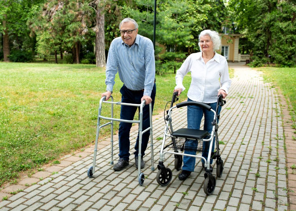 Displayed are two seniors walking along a path with their walkers as support.